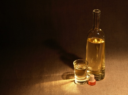 Open bottle of wine or vodka near wineglass on canvas surface under beam of lightの写真素材