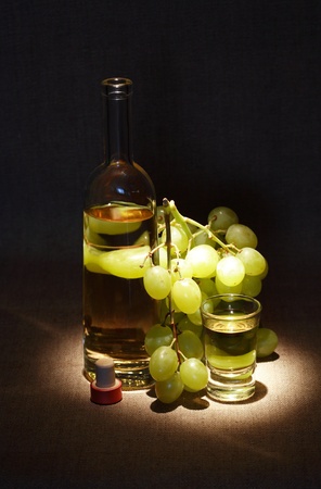 Bunch of grapes near bottle of white wine and wineglass on dark backgroundの写真素材