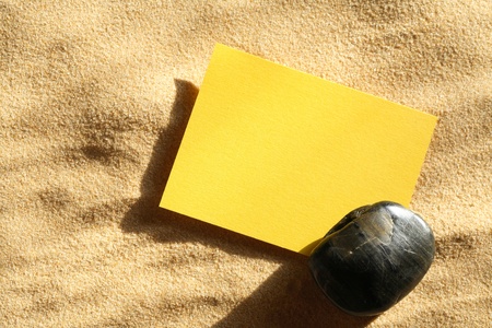 Closeup of blank yellow paper sheet under stone on sand surface
