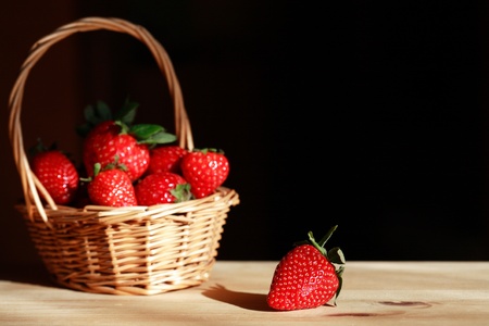 Wicker basket full of strawberries on wooden surface under sunbeam. Good background with free space for textの写真素材