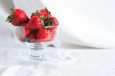 Transparent glass vase full of red strawberries on white textile background with free space for textの写真素材