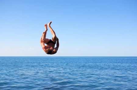 Young strong man doing somersault between blue sky and seaの写真素材