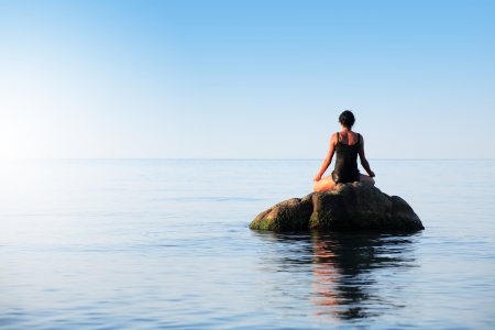 Svelte adult woman doing yoga on big stone in the seaの写真素材