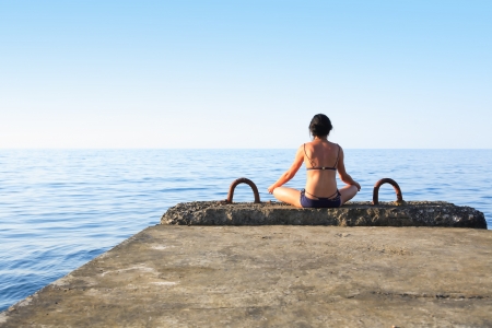 Svelte mature woman sitting on pier near sea and looking to horizonの写真素材