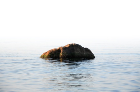 One big stone in tranquil sea under blank white space for text