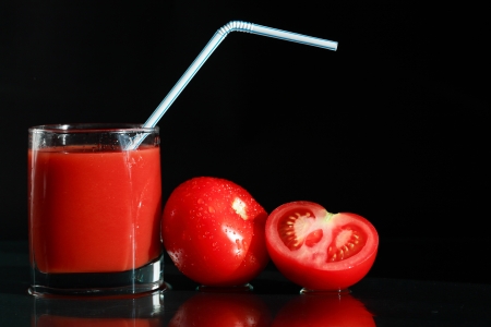 Glass of tomato juice near tomatoes on black backgroundの写真素材