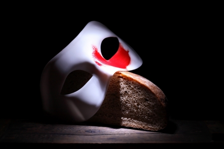 Roman Empire concept. White mask with red spot lying on bread on black background