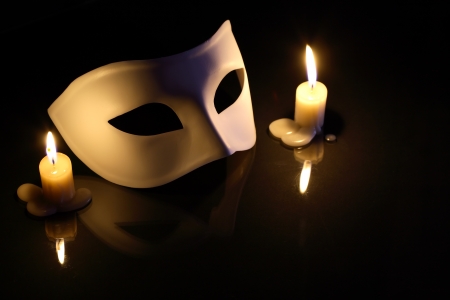 White mask between lighting candles on dark backgroundの写真素材