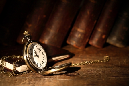 Vintage pocket watch on wooden surface against old booksの写真素材