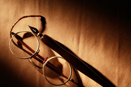 Old spectacles and ink pen on paper surface under beam of lightの写真素材