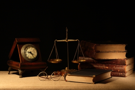 Vintage wooden clock near brass weight scale and books on dark backgroundの写真素材
