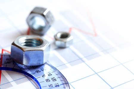 Few screw nuts near ruler on paper background with business chart