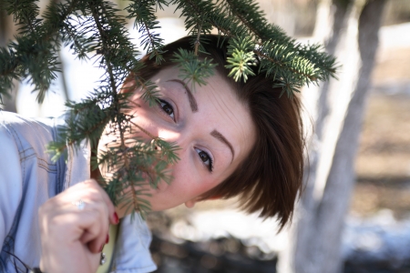Portrait of beautiful young girl under spruce tree and looking to cameraの写真素材