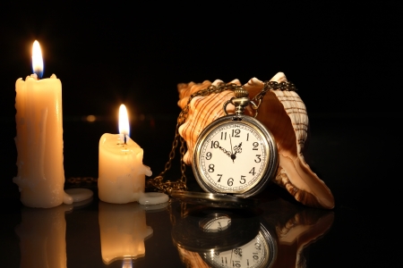 Vintage pocket watch near lighting candles and shellの写真素材