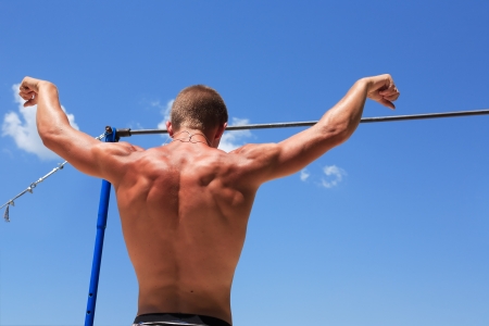 Young strong athlete standing before horizontal bar against blue skyの写真素材