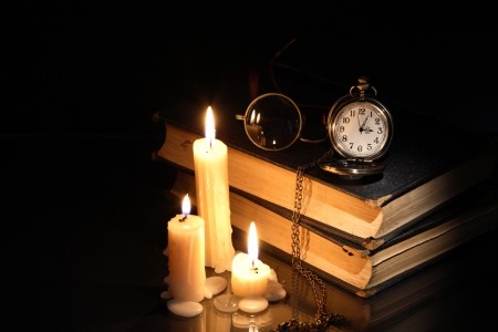 Vintage pocket watch and spectacles on old books near lighting candlesの写真素材