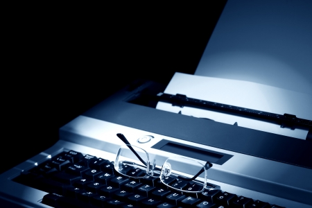 Eyeglasses on keyboard of electric typewriter with blank paperの写真素材