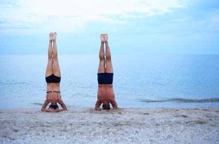 Svelte mature woman and strong man standing on head near seaの写真素材