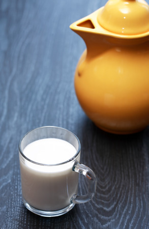 Glass full of milk near yellow pitcher on dark wooden tableの写真素材