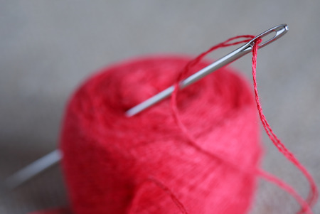 Sewing concept. Extreme closeup of steel needle with red threadの写真素材