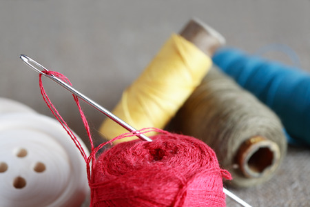 Sewing concept. Closeup needle against spools of thread near wooden buttons