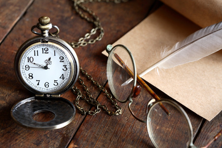 Old spectacles near watch and feather on nice old wooden backgroundの写真素材