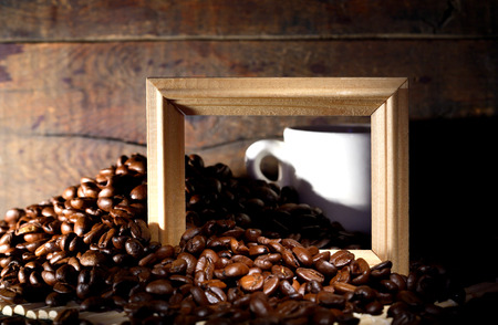 Heap of coffee beans and cup with picture frame on old wooden table の写真素材