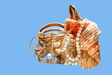 Beautiful conch shell with various jewelry on blue background with reflectionの写真素材