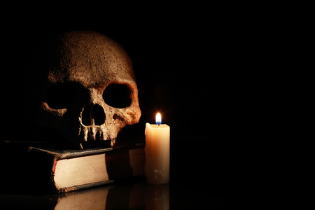 One human skull on old book near lighting candle on dark backgroundの写真素材