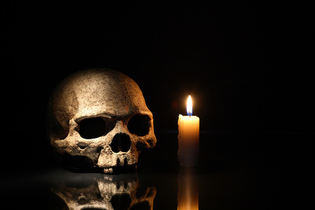 Death concept. One human skull near lighting candle on dark backgroundの写真素材