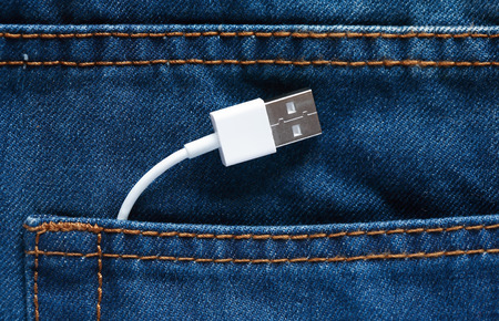 Modern technology. White USB-cable inside pocket of blue jeans