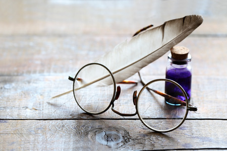 Art concept. Closeup of old spectacles near quill and ink-pot on wooden tableの写真素材
