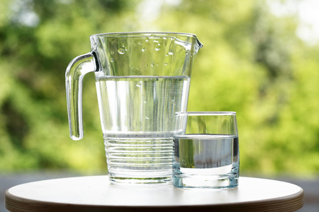 Glass of water near jug on green nature backgroundの写真素材
