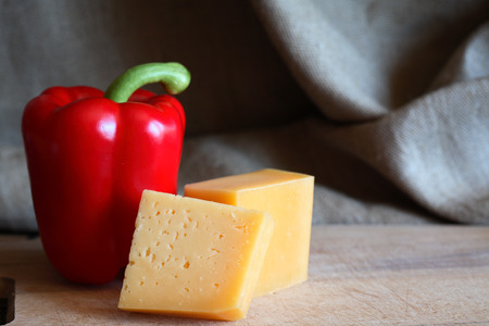 Still life with red sweet pepper near cheese on wooden boardの写真素材