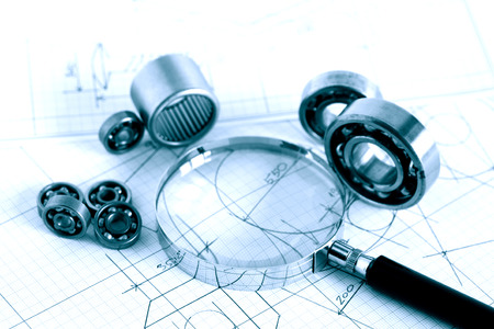 Engineering concept. Closeup of magnifying glass near ball bearings on blueprint with draftの写真素材