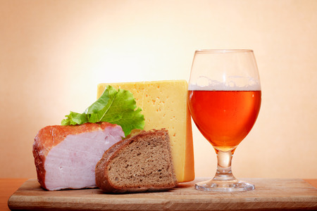 Glass of beer near cheese and meat against wall with spot of lightの写真素材