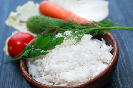 Nice wooden bowl with boiled rice near raw vegetablesの写真素材