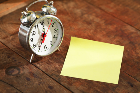 Alarm clock near blank sticky note on nice old wooden backgroundの写真素材