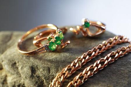 Gold ring with emerald near chain on gray stone against nice dark backgroundの写真素材