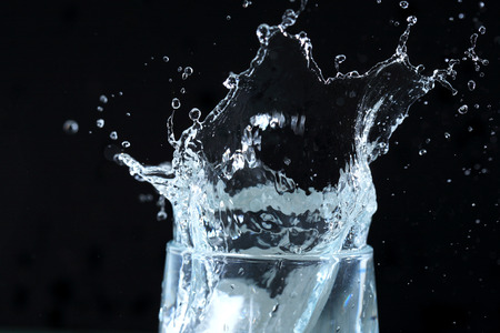 Glass with splashing water on dark background
