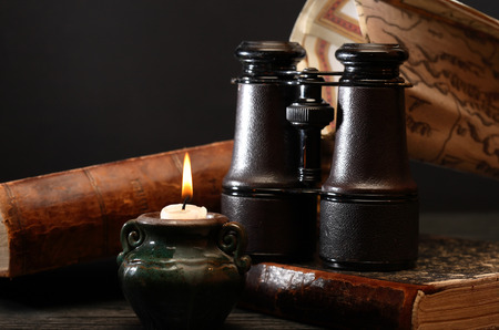 Vintage still life. Old binoculars and books near lighting candleの写真素材