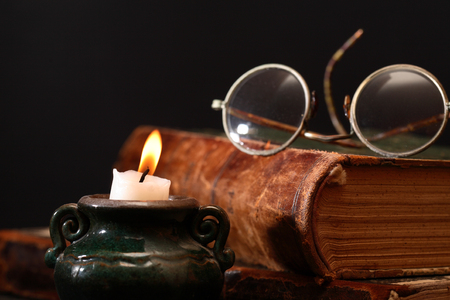Old spectacles on book near lighting candleの写真素材