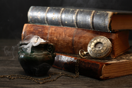 Old pocket watch on book near extinguished candle with smokeの写真素材