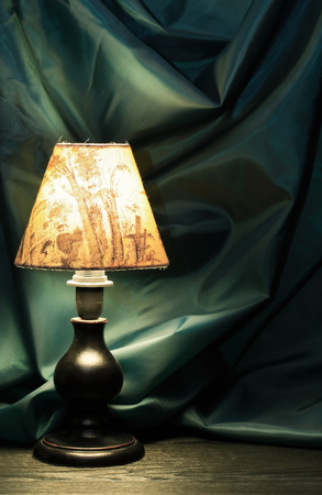Glowing vintage table lamp with lampshade against green textileの写真素材