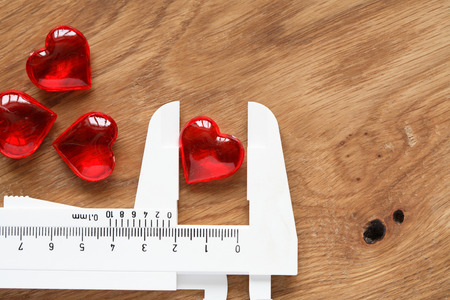 Love or cardiology concept. Red glass heart in white caliper on wooden backgroundの写真素材