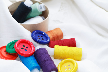 Set of colored thread and buttons on white textile