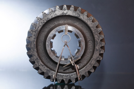 Industrial concept. Divider near old gear on glass surface against gray backgroundの写真素材