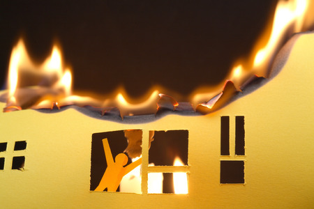 Paper man in window of burning house on dark backgroundの写真素材