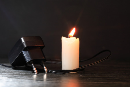 Electric charger with cable near lighting candle on dark background
