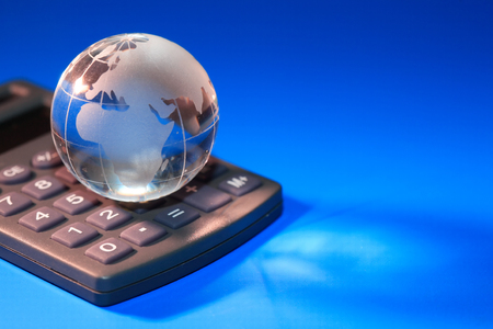 Glass globe on calculator against blue background with free spaceの写真素材